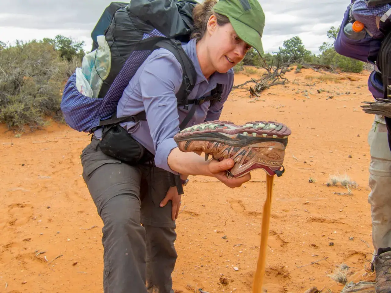 A hiker shakes sand from a shoe, demonstrating the challenge of finding the best shoes for hiking in sand.