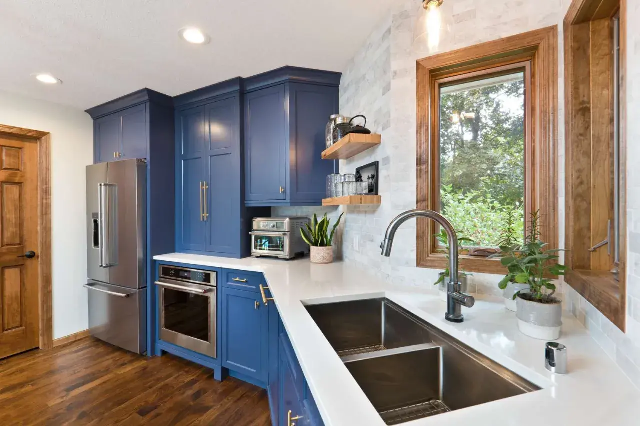 Stylish kitchen sink styling with a modern faucet, double basin sink, and a window overlooking greenery. Blue cabinets and stainless steel appliances complete the look.