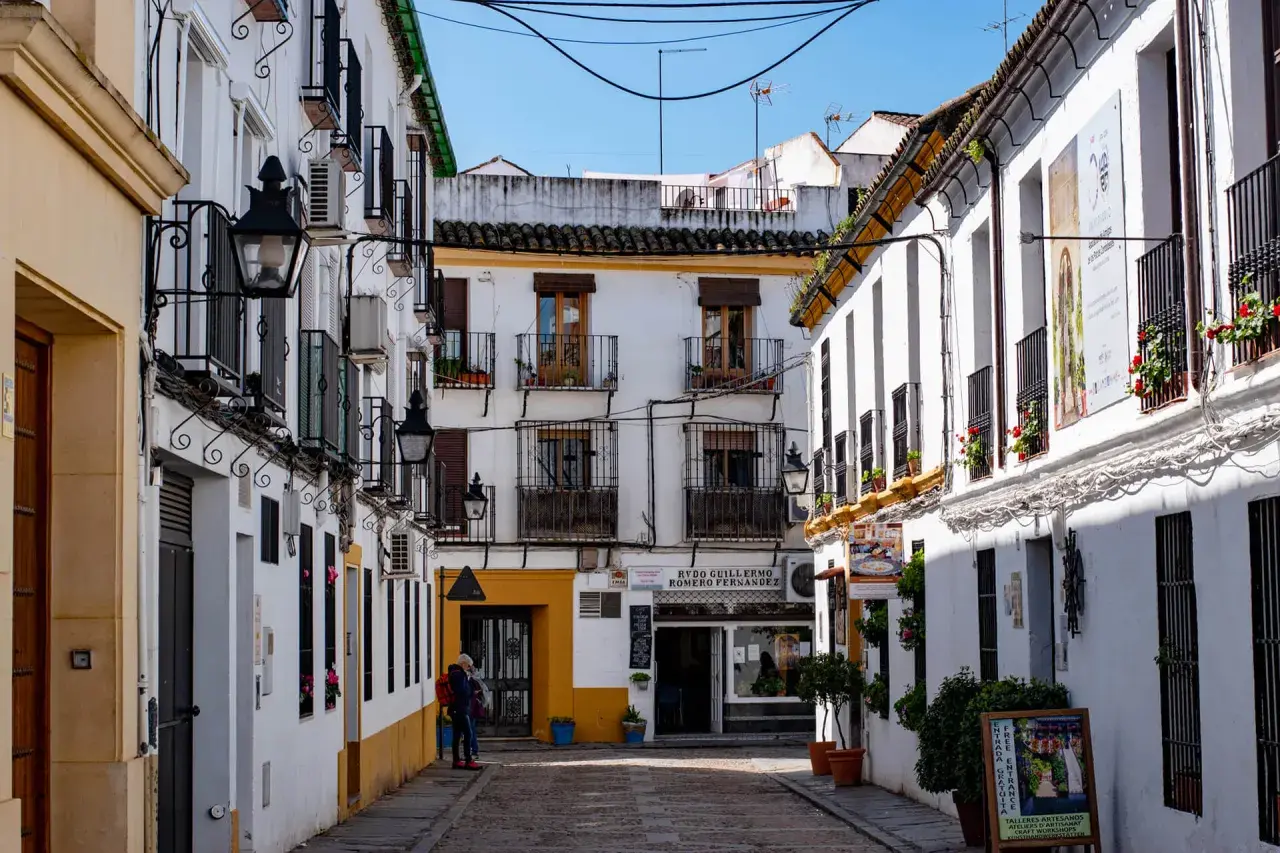Callejuela cordobesa con casas blancas, balcones de hierro y faroles. Un cartel anuncia "Entrada Gratuita", ideal para saber qué ver en Córdoba gratis.