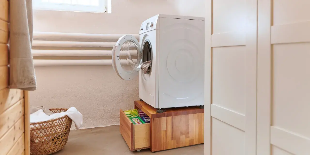 Waschmaschinen Podest selber bauen: Eine weiße Waschmaschine steht auf einem Holzpodest mit Schublade, darin Waschmittel.