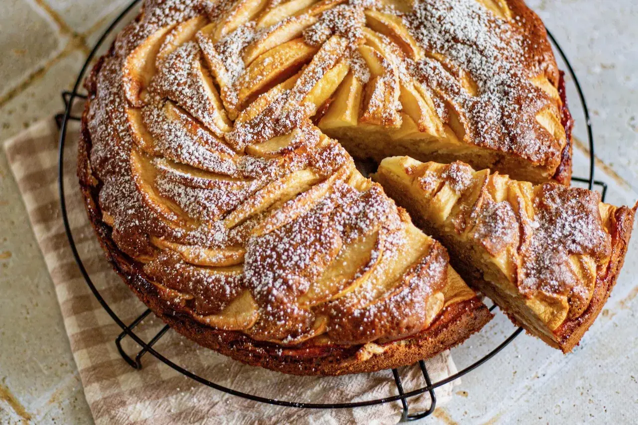 Gâteau mascarpone pommes, une tranche coupée, saupoudré de sucre glace. Un délice doré et moelleux.