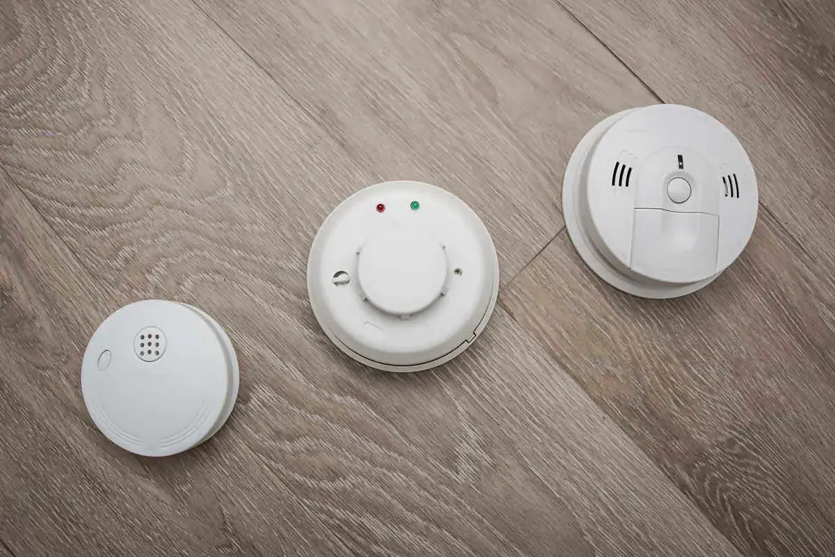Trois détecteurs de fumée blancs sur un parquet. L'obligation d'installer un détecteur de fumée en entreprise est une mesure de sécurité essentielle.