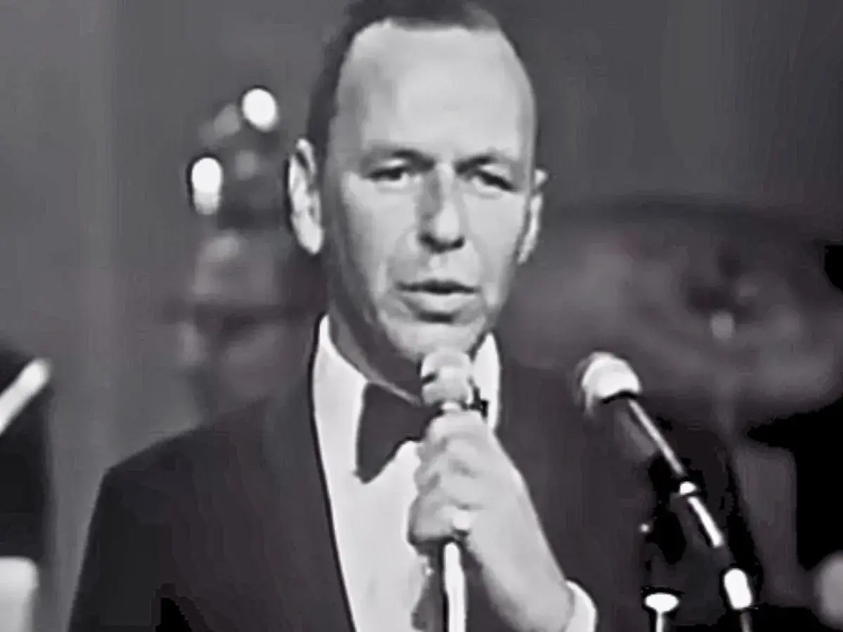 Frank Sinatra śpiewa "Fly Me to the Moon lyrics", ubrany w smoking.