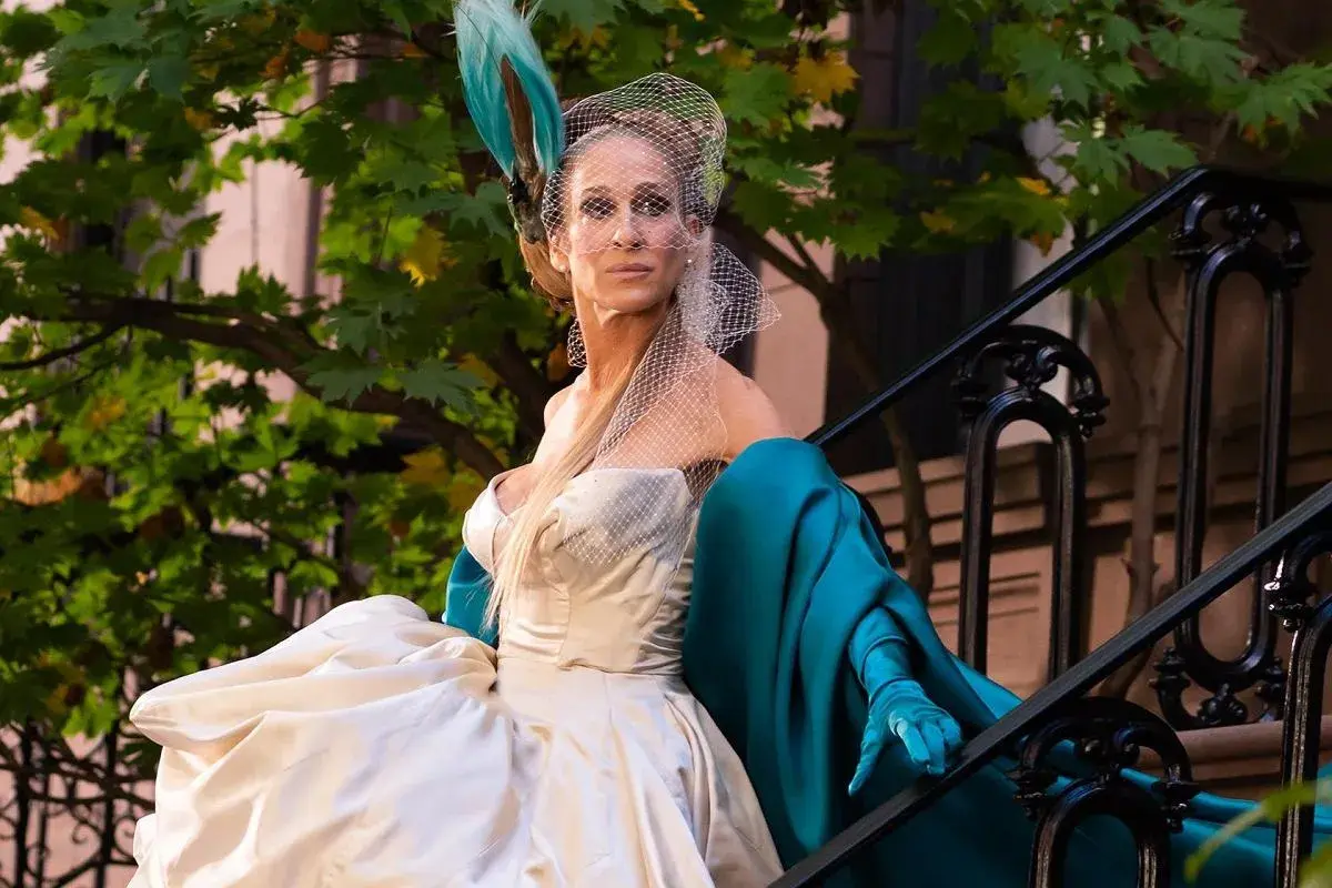 Carrie Bradshaw w białej sukni i turkusowym płaszczu, z welonem na głowie, siedzi na schodach. I tak po prostu.