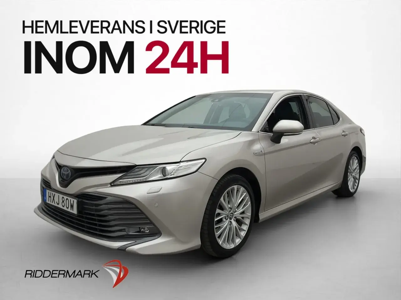 En silverfärgad, begagnad Toyota Camry hybrid visas framifrån. Hemleverans inom 24 timmar i Sverige.