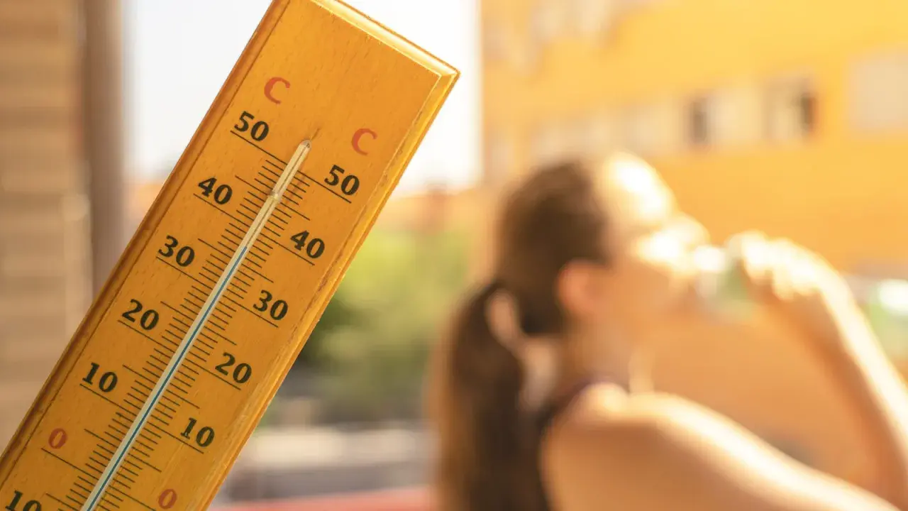 En termometer visar över 30 grader. En person dricker ur ett glas. Frågan är hur varmt får det vara på jobbet?