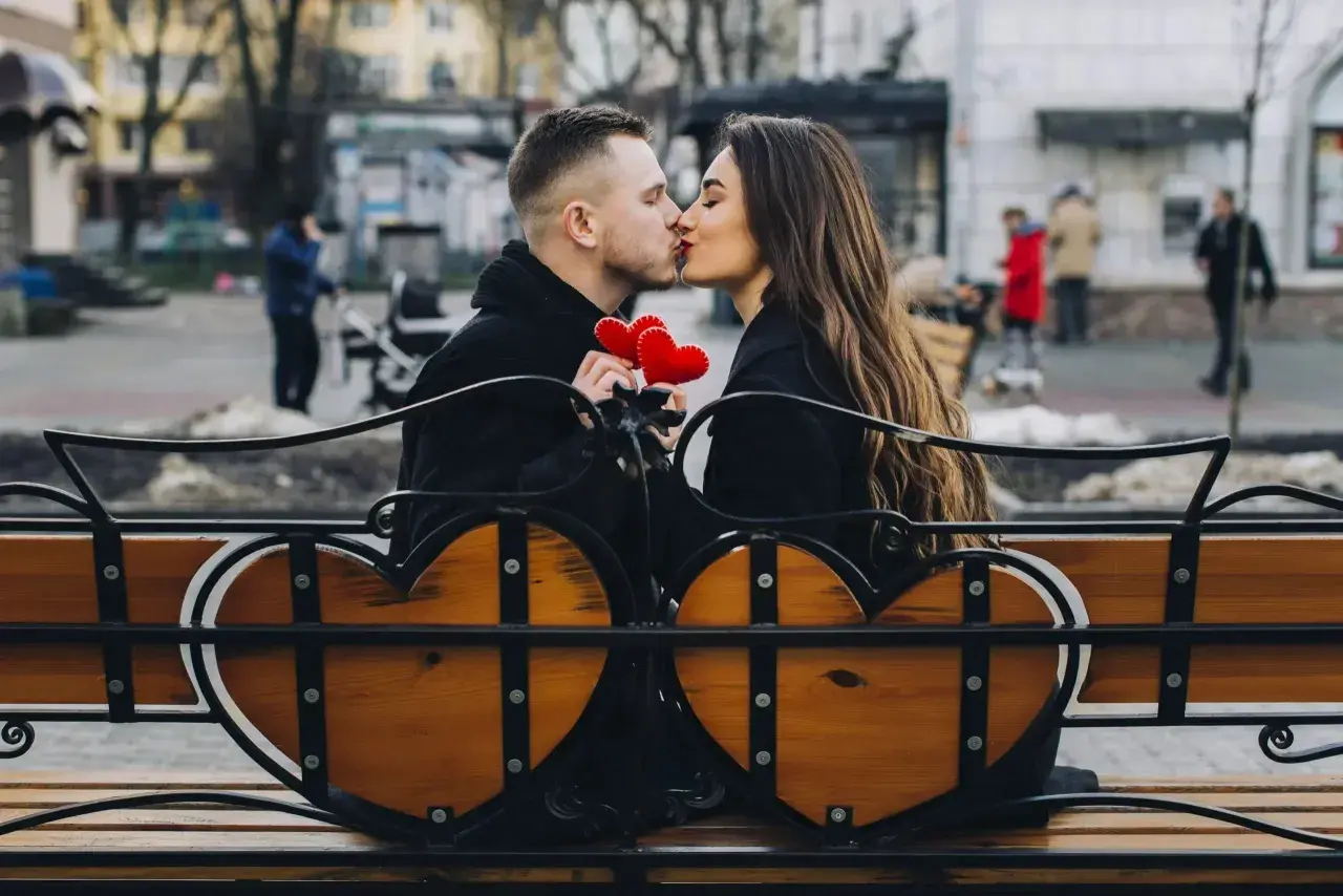 Para spędza romantyczny czas na ławce w kształcie serca, trzymając czerwone serduszka. To świetny pomysł, co można robić z chłopakiem poza domem.