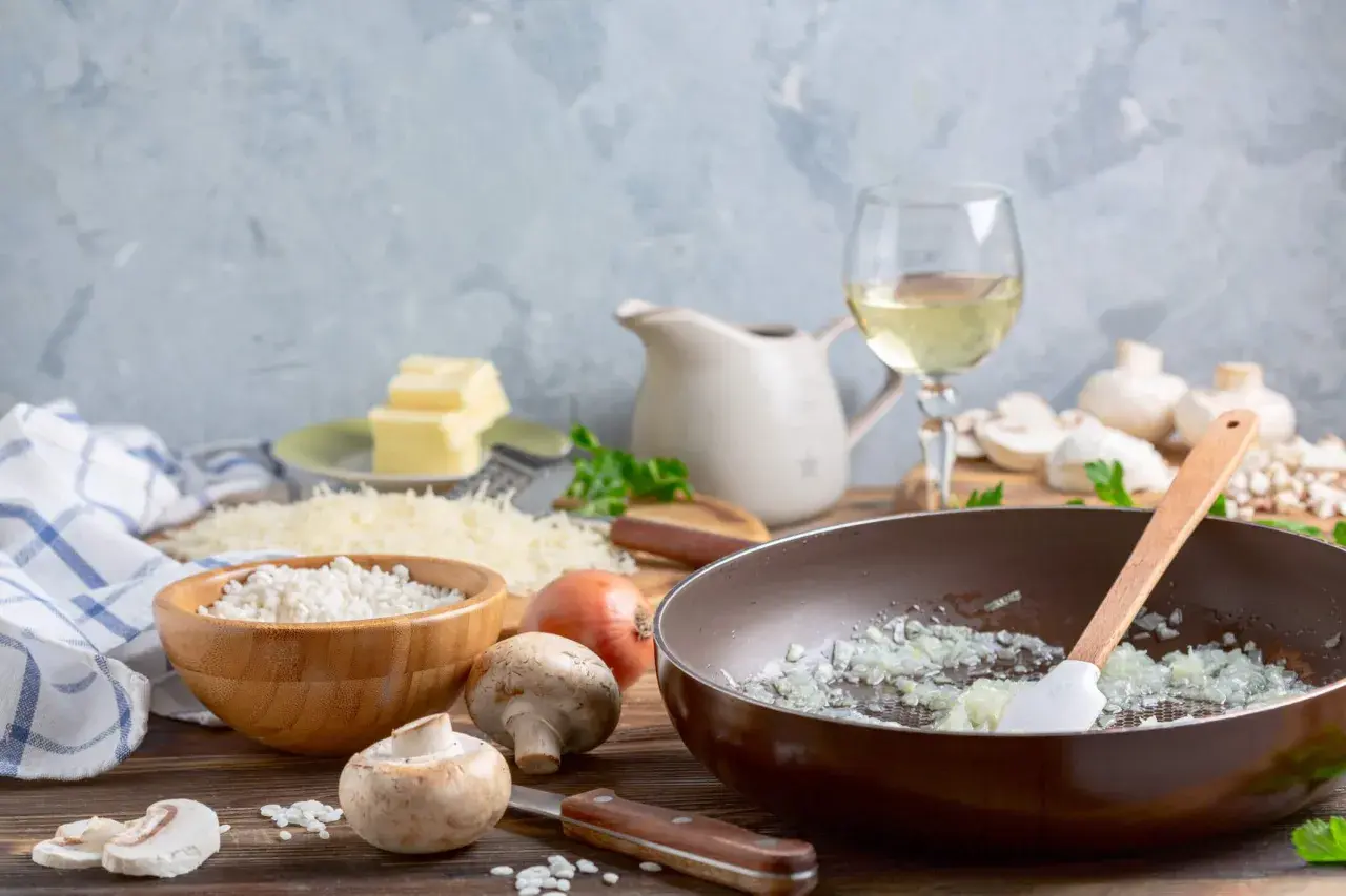 Préparation d'un risotto aux champignons, avec riz, oignons, champignons, parmesan, beurre et un verre de vin blanc.