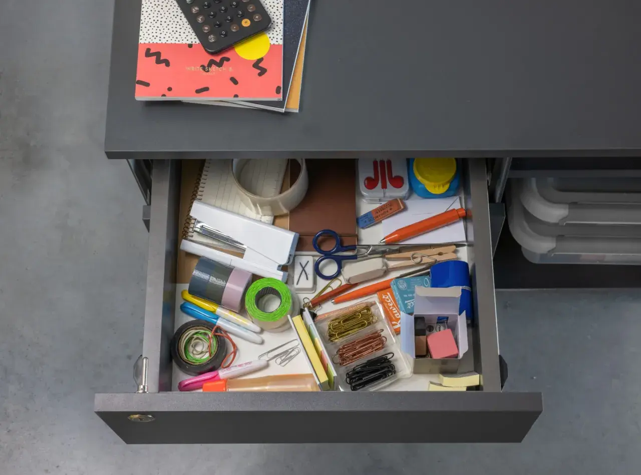 Szukając odpowiedzi na pytanie "decluttering co to?", widzimy szufladę pełną artykułów biurowych: zszywacz, taśmy, nożyczki, spinacze, markery i gumki.