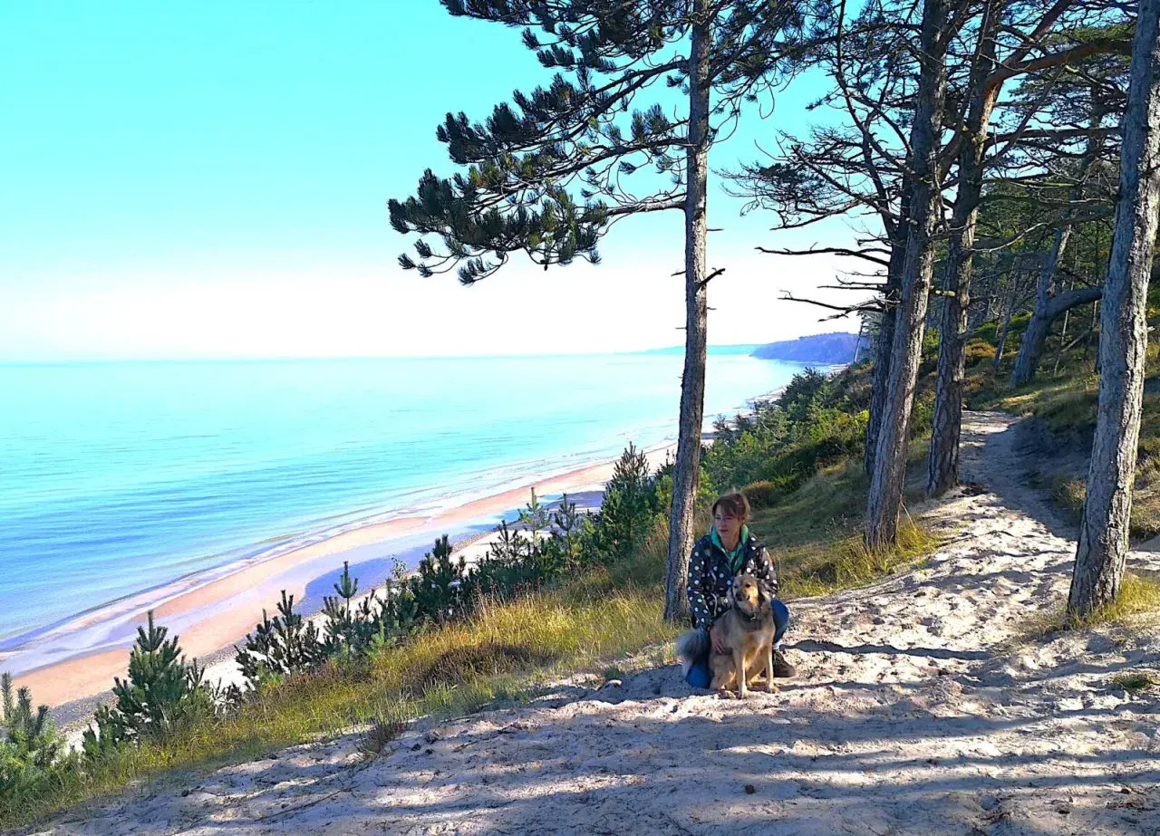 Frau mit Hund auf einem sandigen Pfad mit Blick auf die polnische Ostsee.