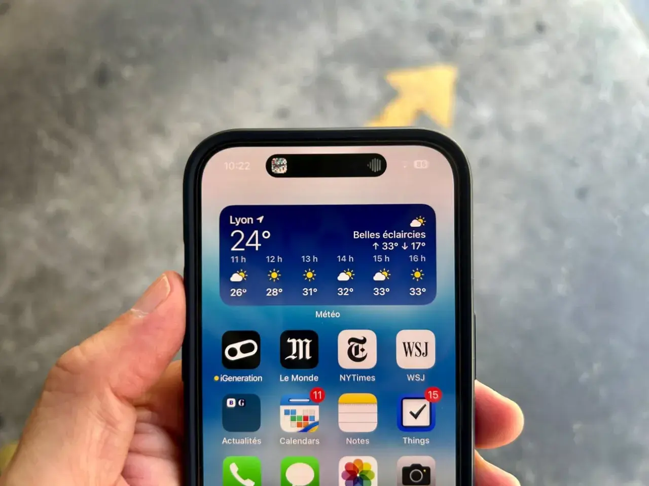 iPhone avec la Dynamic Island affichant la météo à Lyon. La barre d'état montre l'heure et le niveau de batterie.