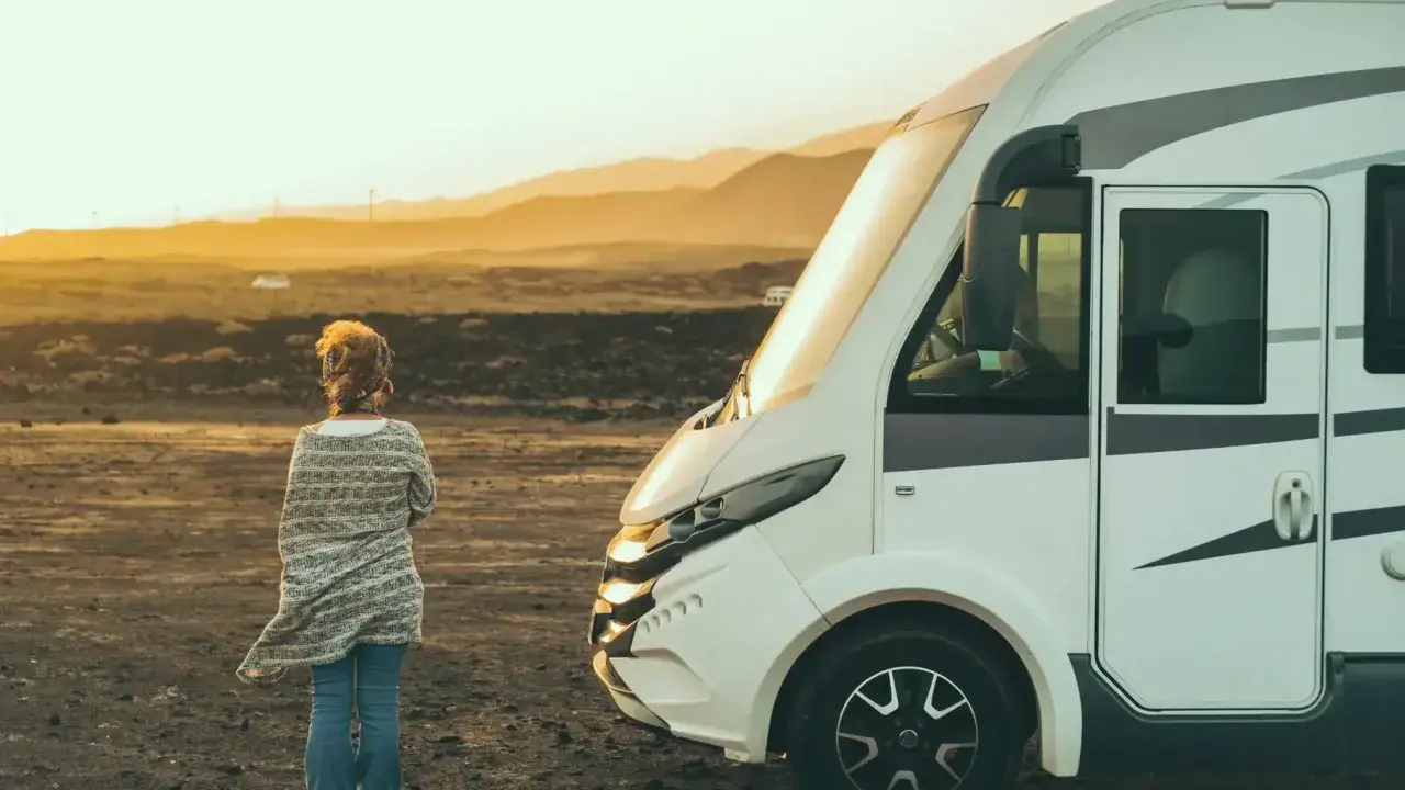 Une femme seule face à un camping-car dans un paysage désertique au coucher du soleil. Un lieu à éviter en camping-car pour son isolement.