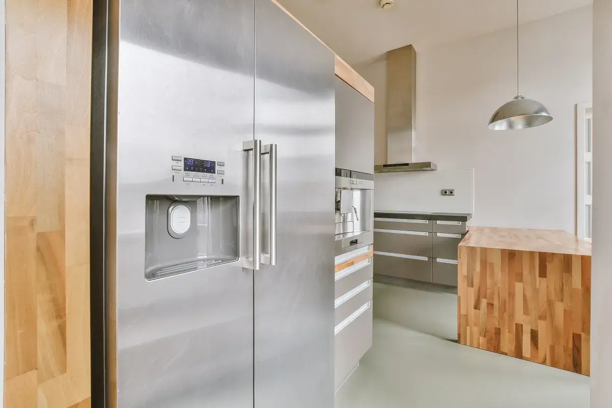 Nowoczesna kuchnia z lodówką w kolorze inox, drewnianą wyspą i stalowymi szafkami.