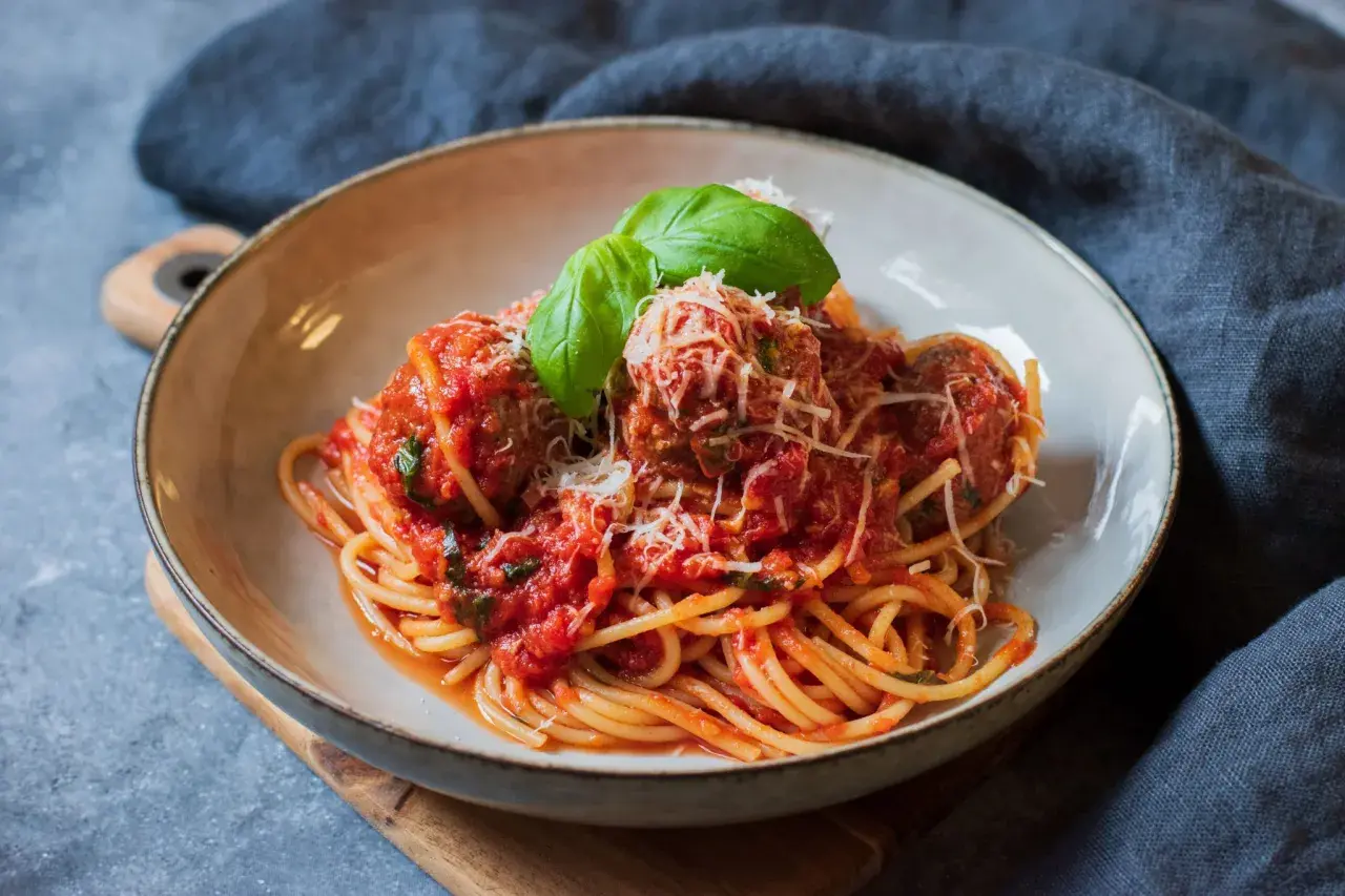En skål med spaghetti och köttbullar i tomatsås, toppad med parmesan och basilika. En klassisk pasta polpette-rätt.