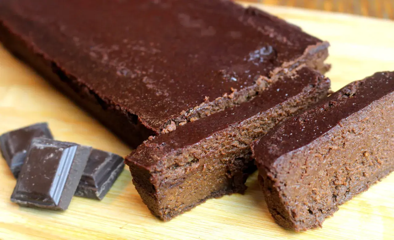 Un délicieux gâteau chocolat compote, coupé en tranches, avec des carrés de chocolat à côté.