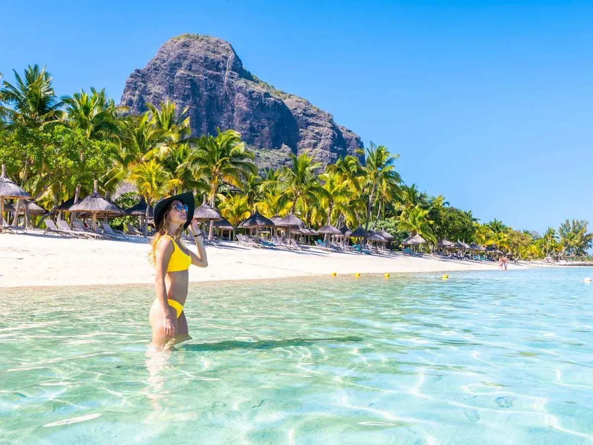 Frau im Bikini genießt das kristallklare Wasser an einem Traumstrand von Mauritius. Palmen und ein Berg im Hintergrund.
