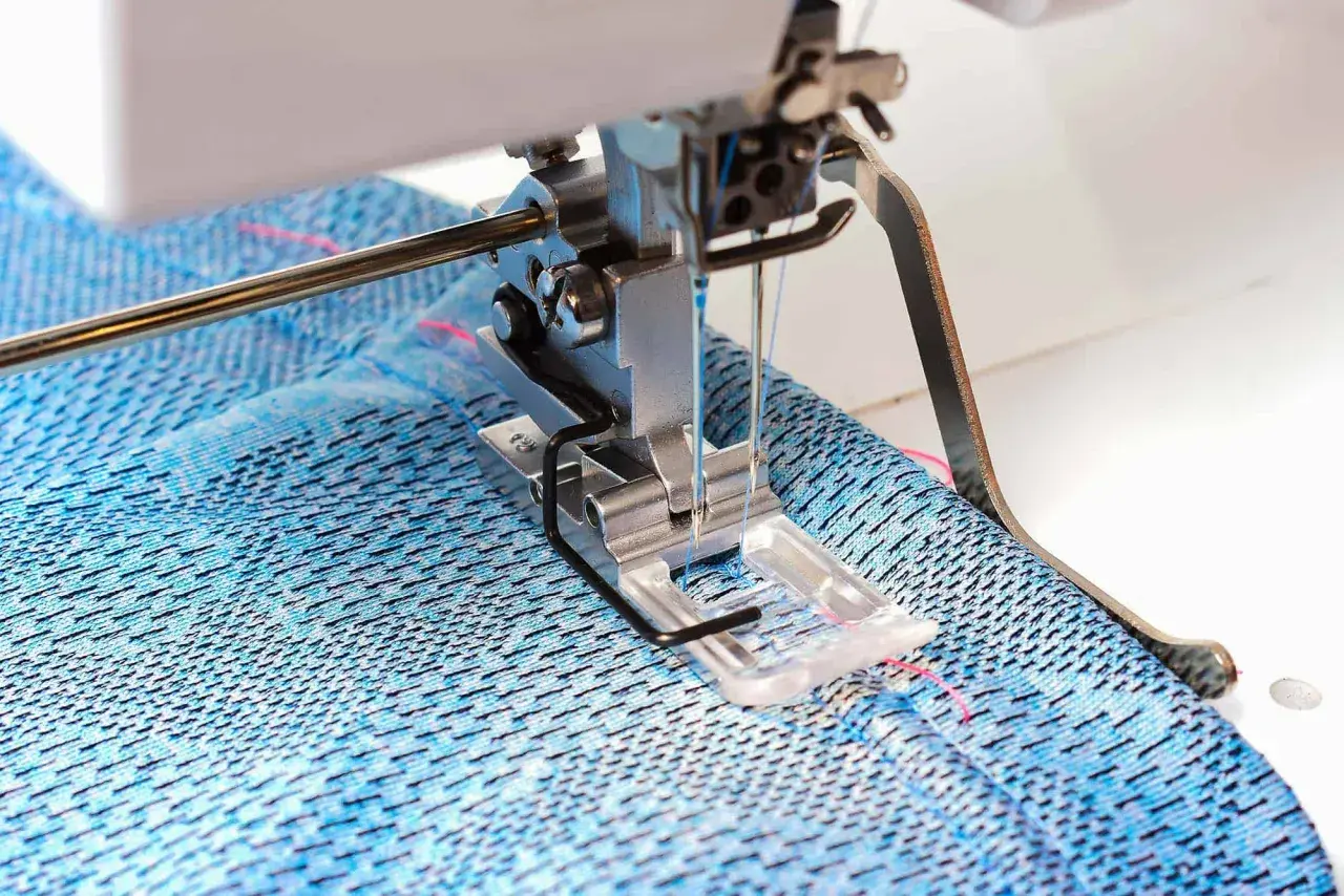 Sewing machine creating a coverstitch hem on blue patterned fabric.