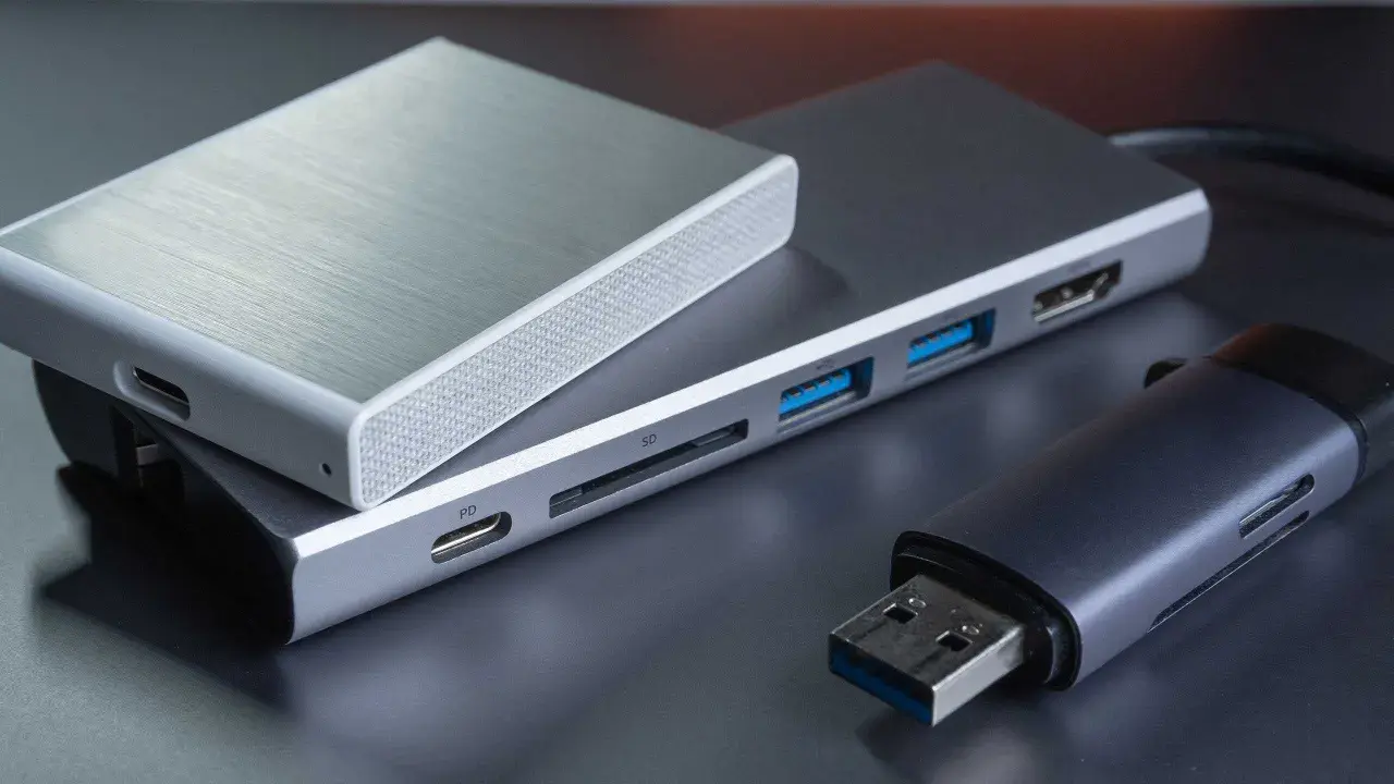Ein silbernes Gehäuse für eine externe Festplatte liegt auf einem USB-Hub mit SD-Kartenleser und mehreren USB-Anschlüssen. Daneben ein USB-Stick.