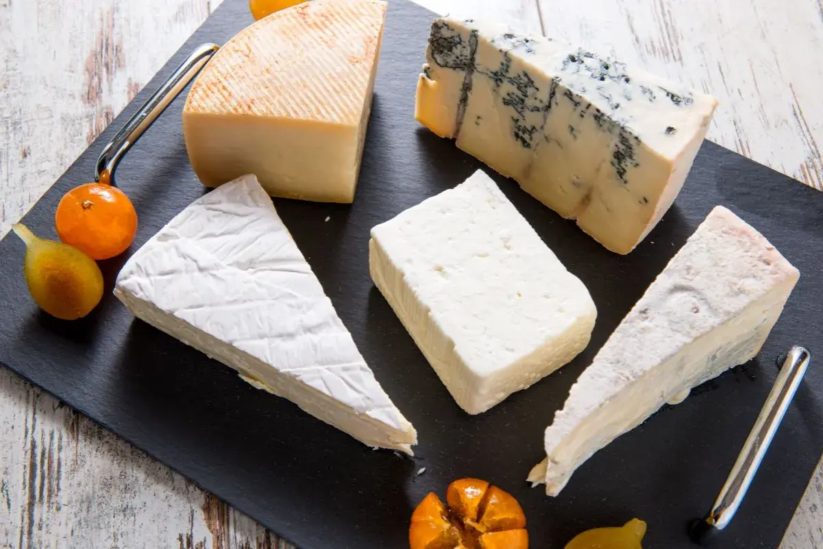 Assortimento di formaggi, tra cui un cremoso formaggio morbido, un erborinato e altri tipi, guarniti con frutta.