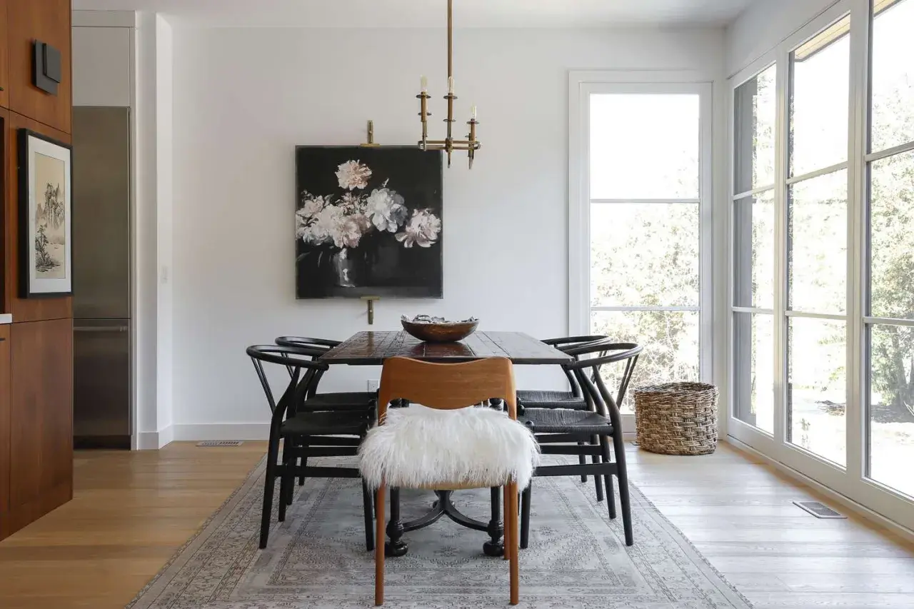 Modern dining room ideas: a dark wood table with black wishbone chairs, a floral painting, and a fluffy white accent chair.