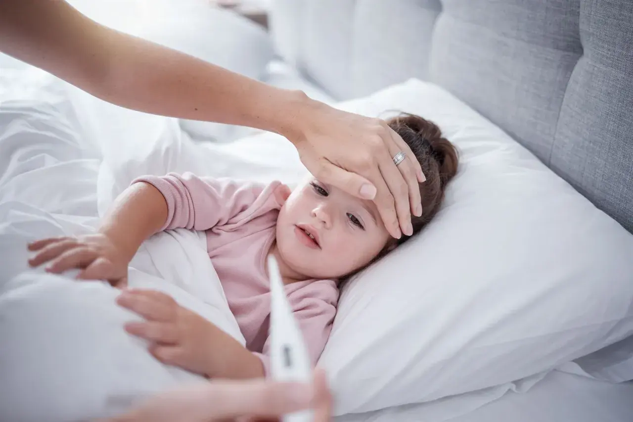 Madre revisa la fiebre de su hija. Si la fiebre persiste, considera el ibuprofeno para bebes.