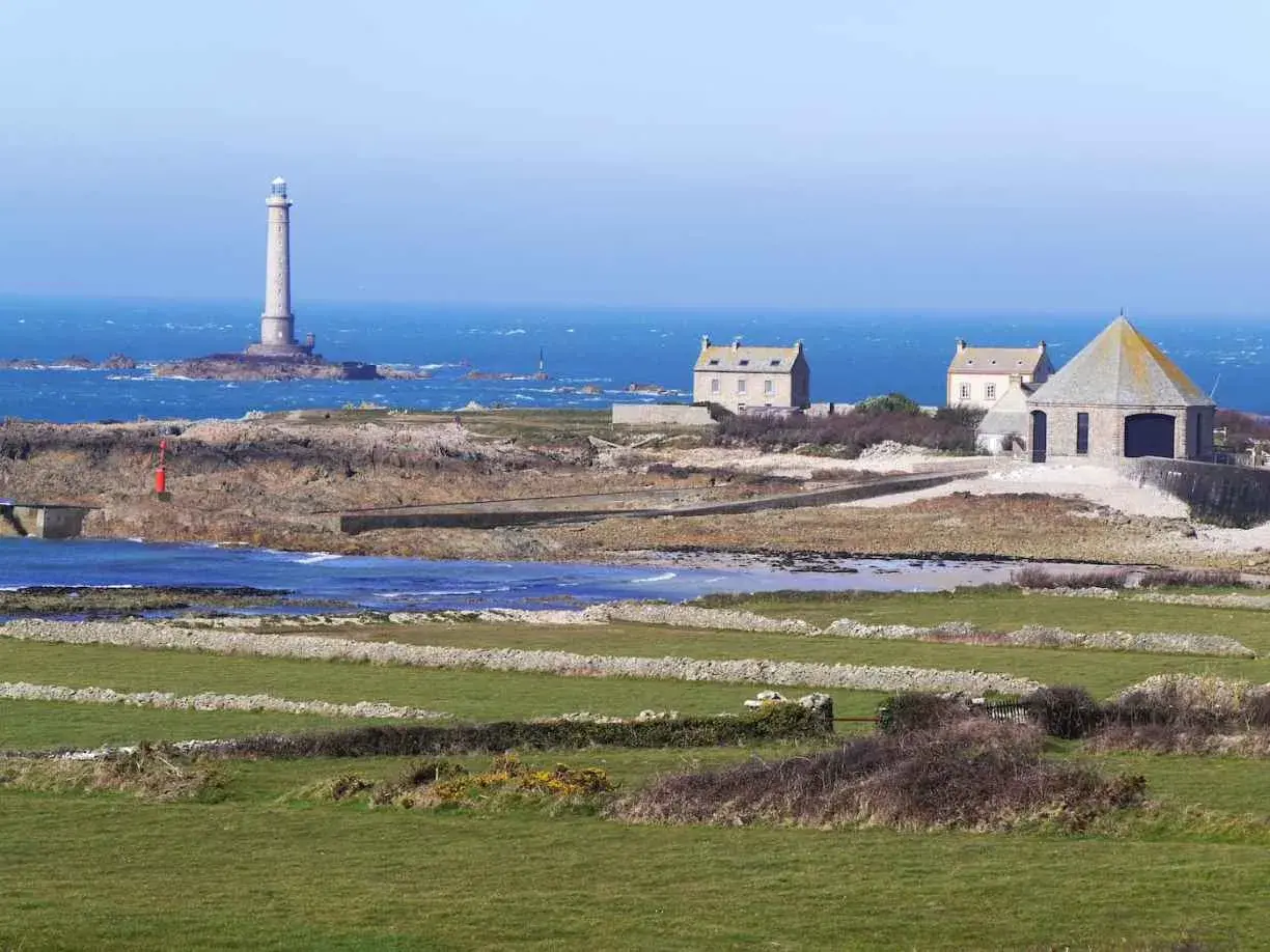 Vue panoramique de la Pointe de la Hague avec son phare emblématique, des maisons de pierre et des champs verdoyants.