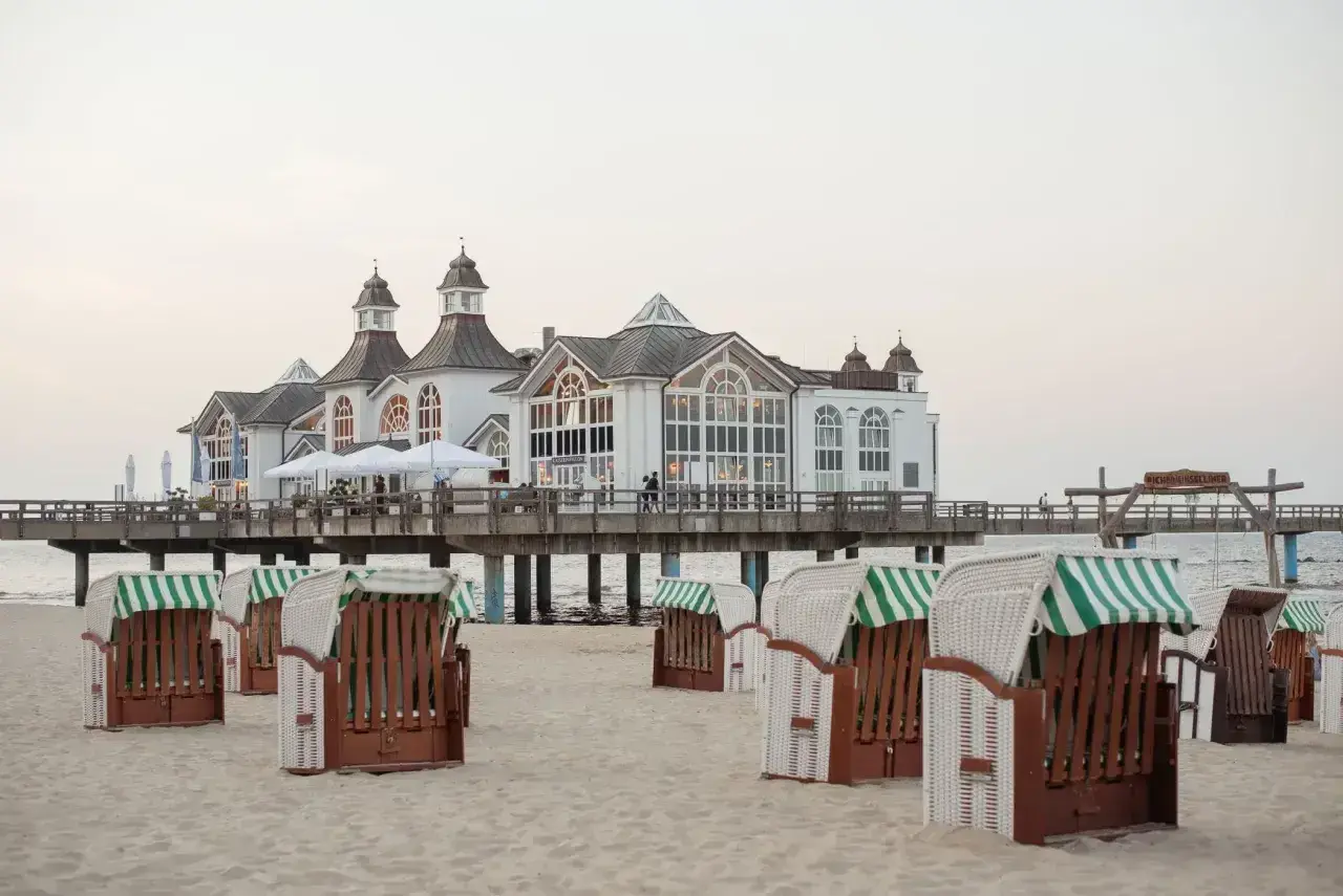 Plaża w Stralsundzie w Niemczech z charakterystycznymi koszami plażowymi i molo z białą budowlą.