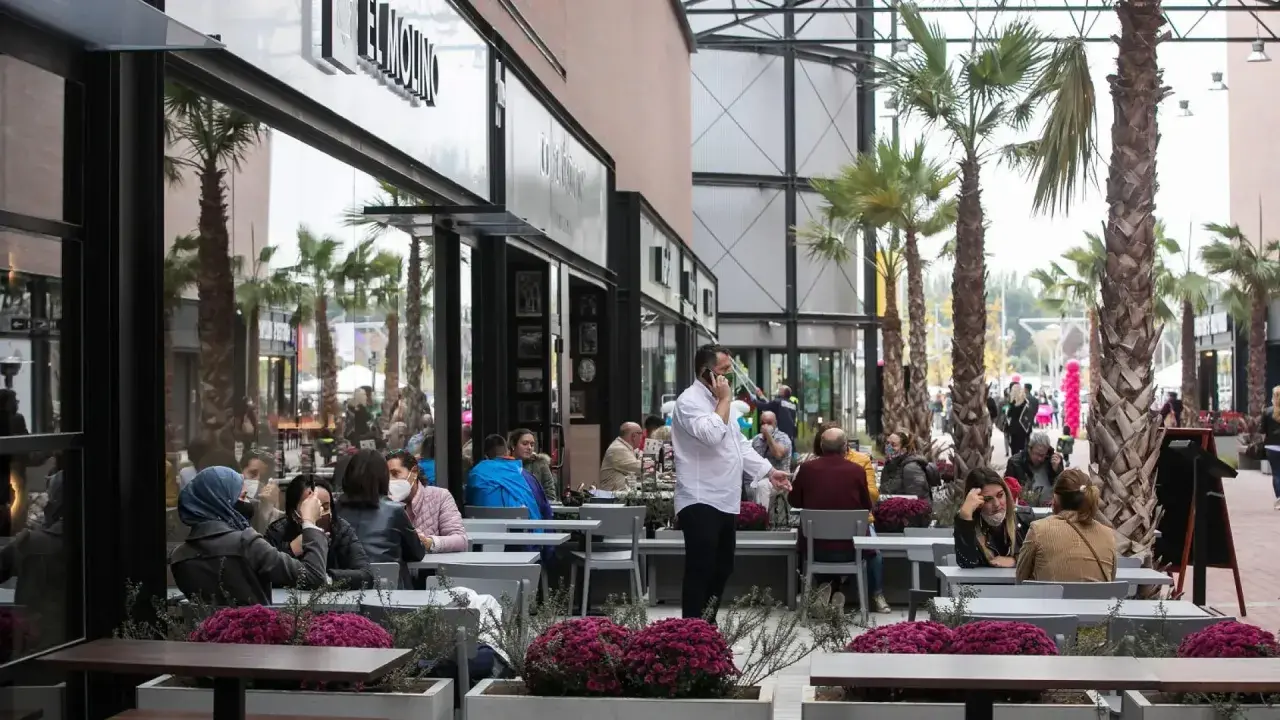 Gente disfrutando en los restaurantes de la torre outlet, rodeados de palmeras y flores.