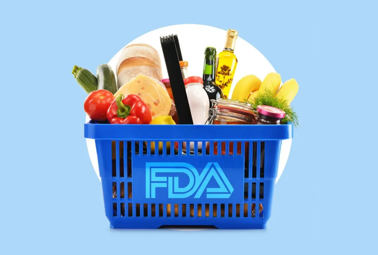 A blue shopping basket filled with groceries, including bread, cheese, and produce, with the FDA logo prominently displayed. This image represents food safety regulations overseen by the FDA and USDA.