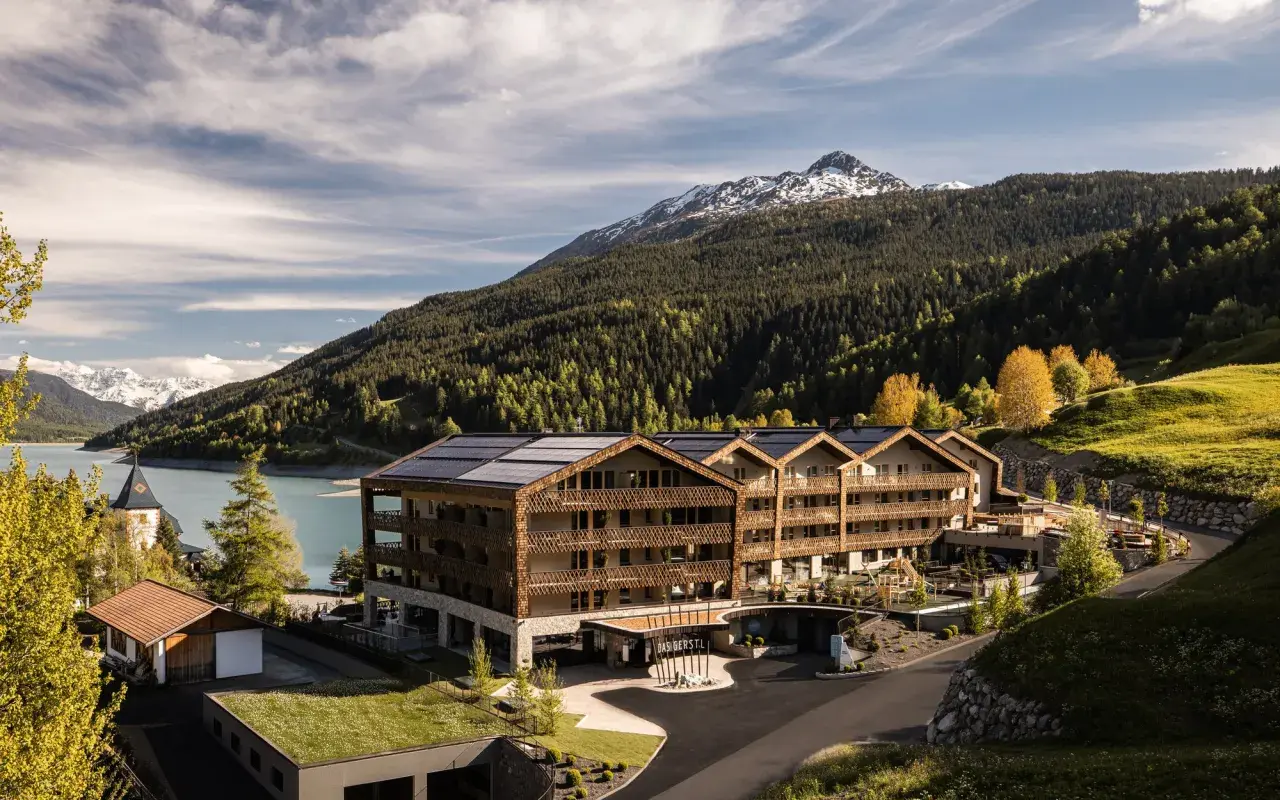 Das Gerstl Family Retreat, un hotel moderno con pannelli solari, si affaccia su un lago alpino e montagne boscose.