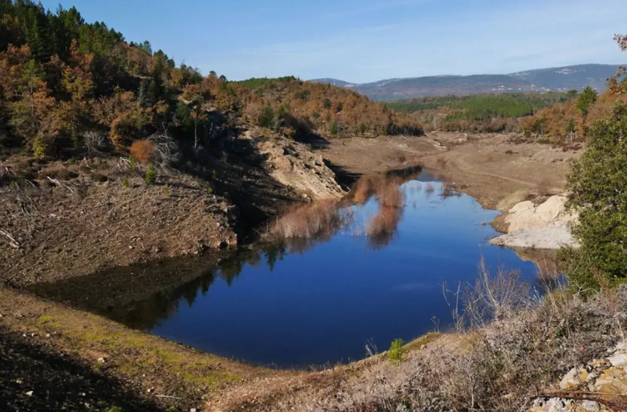 Le lac de Meaulx, aux reflets bleus intenses, est entouré de collines boisées aux couleurs d'automne.