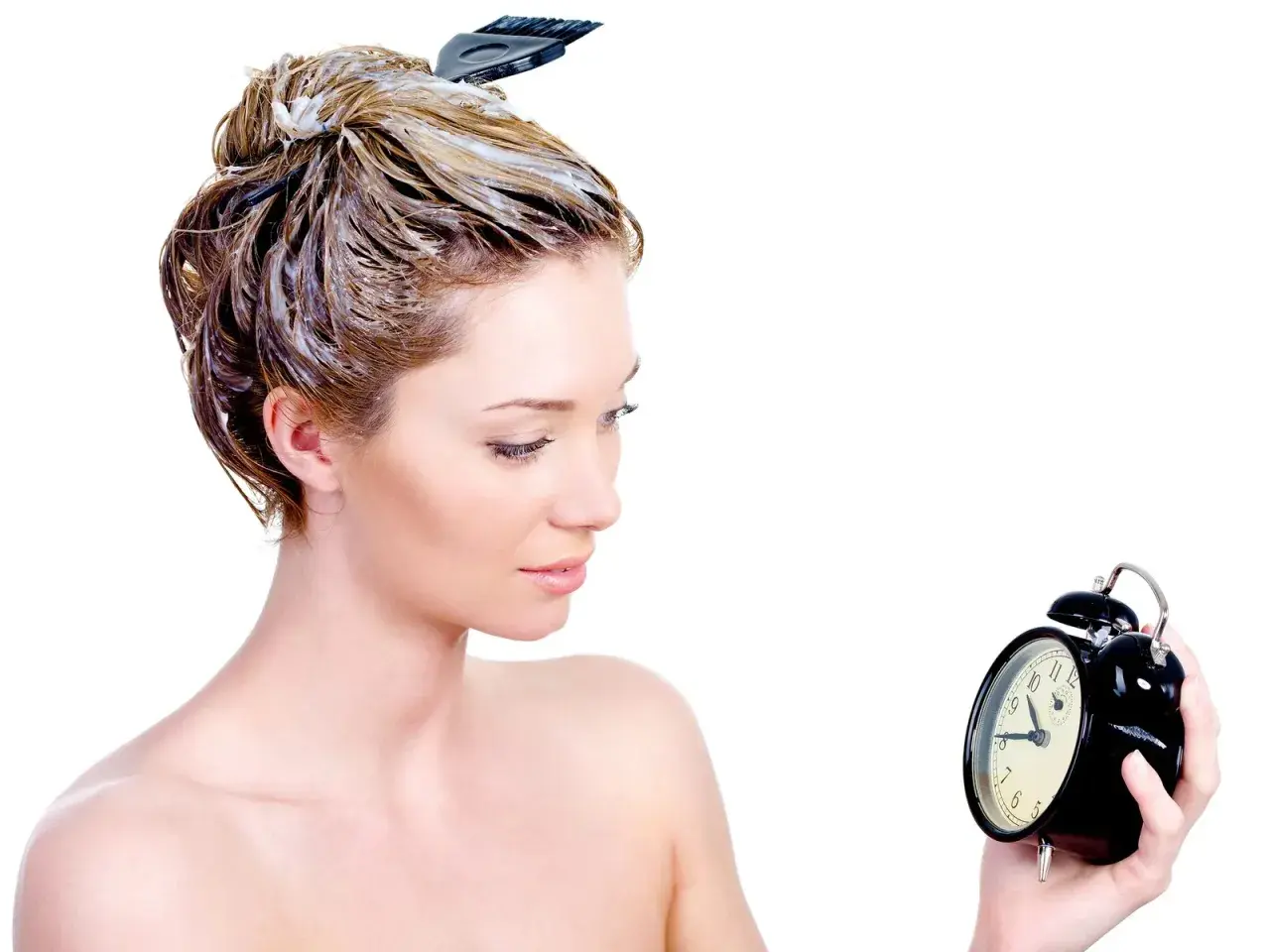 Mujer con tinte en el pelo, mirando un reloj. El tiempo es crucial para un tinte pelo perfecto.
