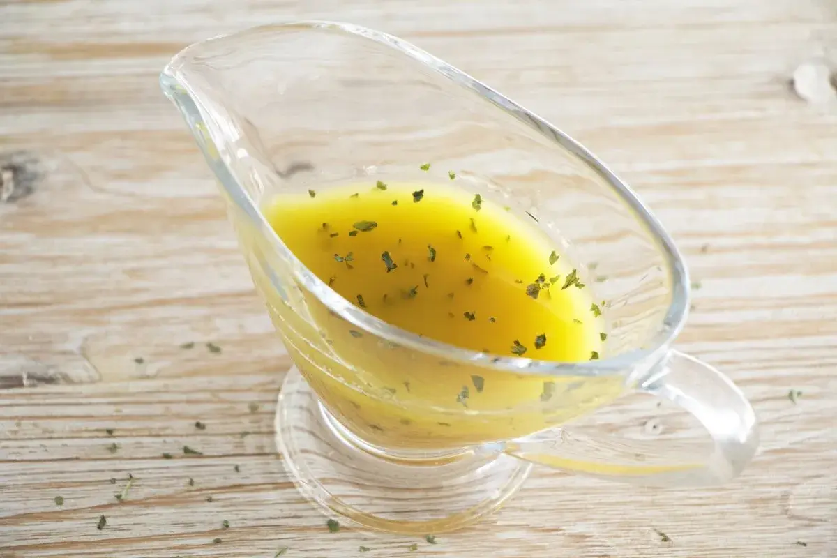 Salsa dorada con hierbas verdes en una salsera de cristal. Perfecta vinagreta de mostaza para realzar tus platos.