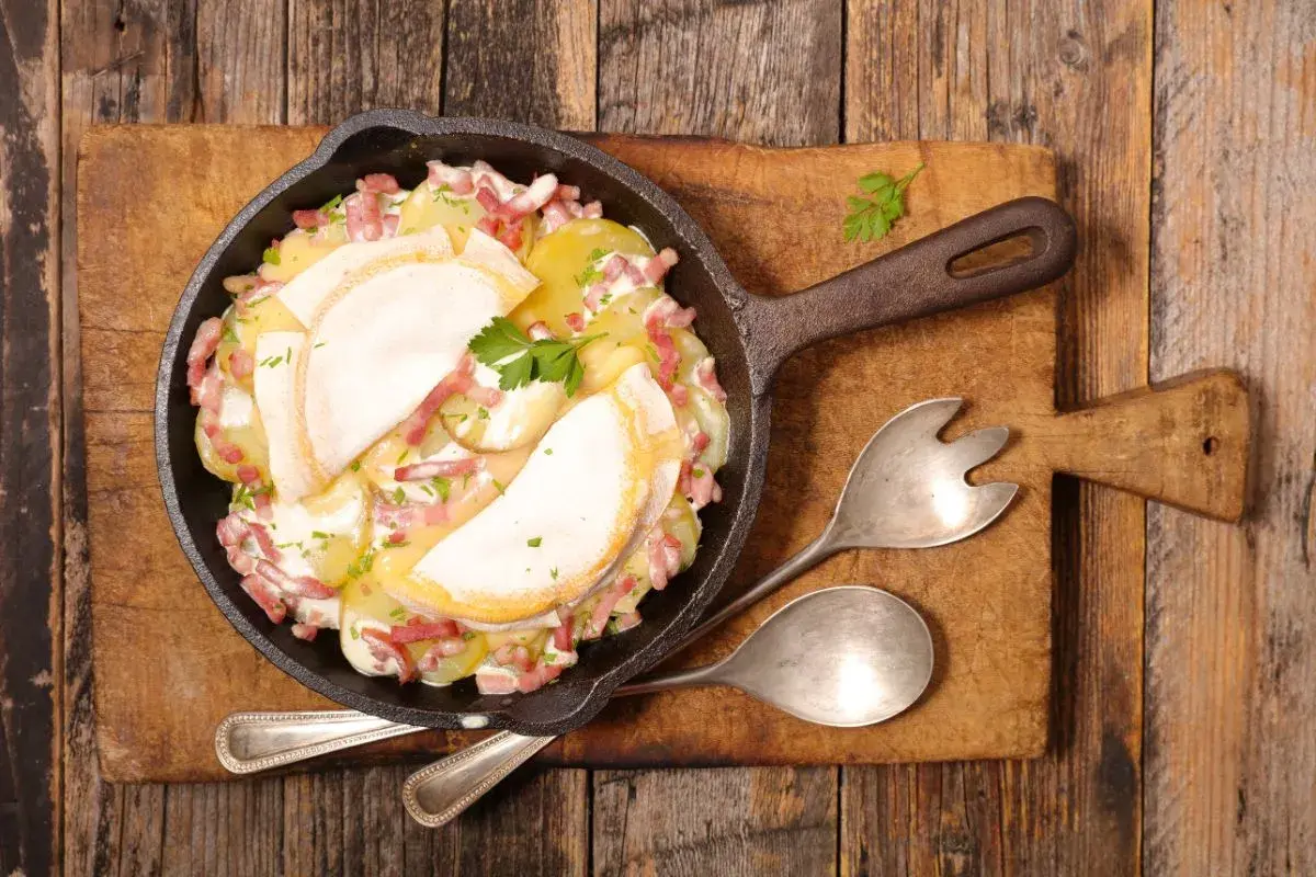 Plat de pommes de terre gratinées avec lardons et fromage fondant, servi dans une poêle en fonte. Un plat avec charcuterie réconfortant.