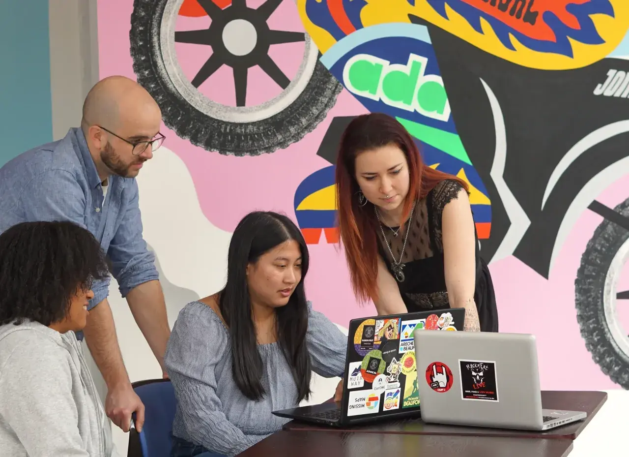 Apprendre comment devenir un développeur web avec des collègues devant un mur coloré.