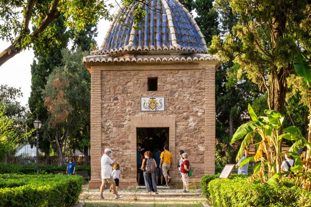 La ermita de Sant Jordi, con su cúpula azul y fachada de piedra, recibe a visitantes entre exuberante vegetación.