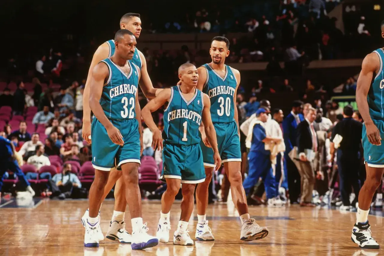Koszykarze Charlotte Hornets, w tym najniższy koszykarz NBA, w turkusowych strojach na boisku.
