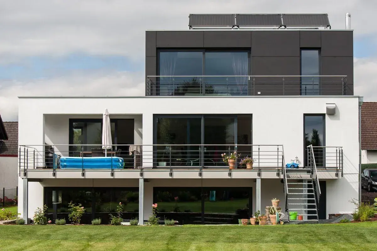 Moderne Hausumbau-Ideen: Vorher-Nachher-Vergleich eines weißen Hauses mit dunklem Anbau, Balkon und Pool.