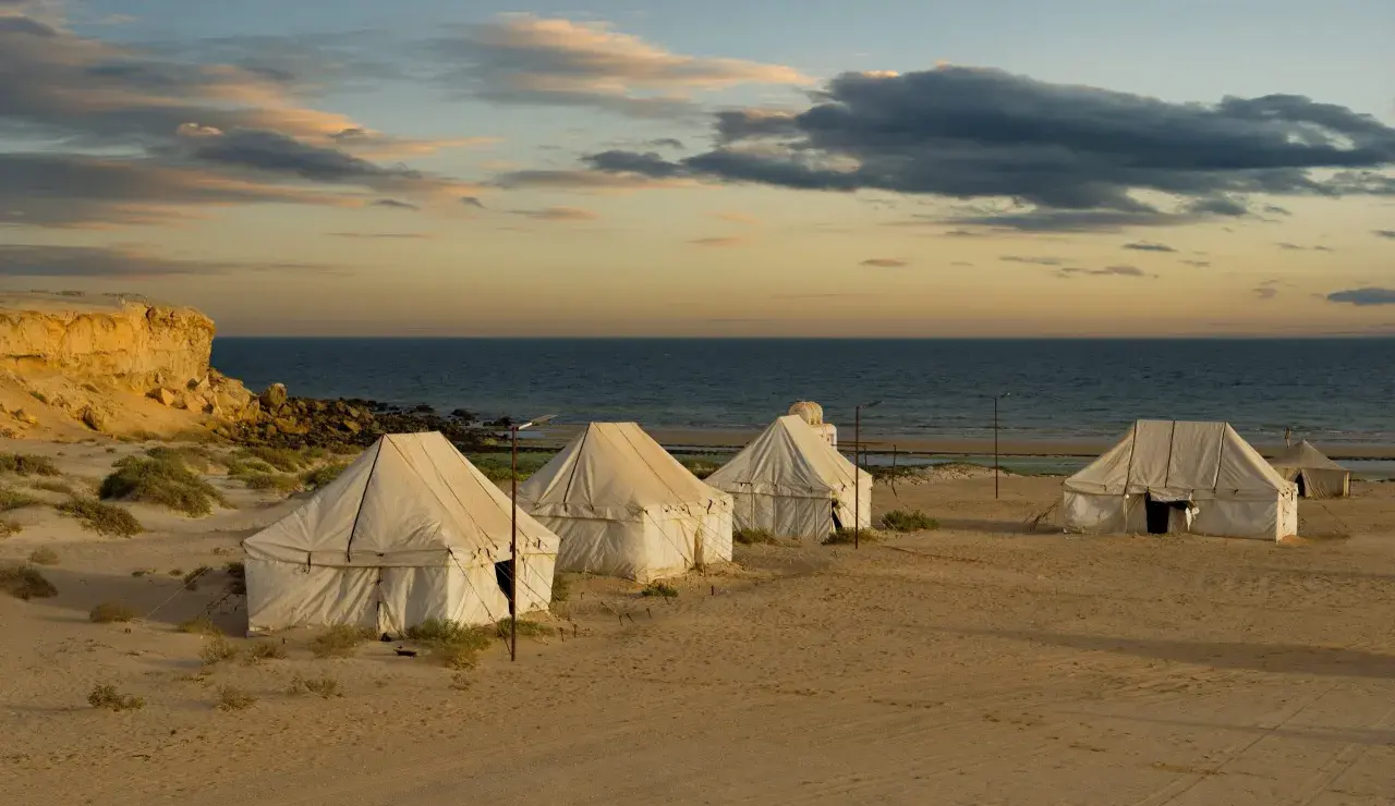 Namioty na piaszczystej plaży nad oceanem o zachodzie słońca.