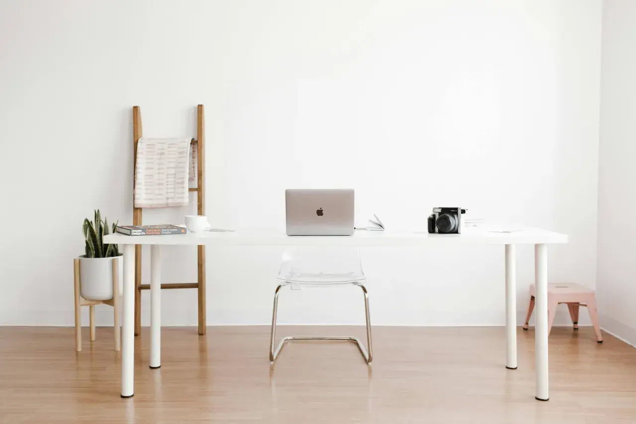 Ein moderner Arbeitsplatz mit einem weißen Schreibtisch, Laptop, Kamera und einer Pflanze. Perfekt für alle, die einen **tisch selber bauen** möchten.