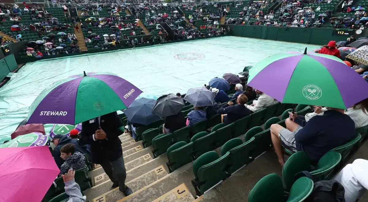 Wimbledon deszcz przerwał mecz. Widzowie siedzą pod parasolami, a kort przykryty jest plandeką.