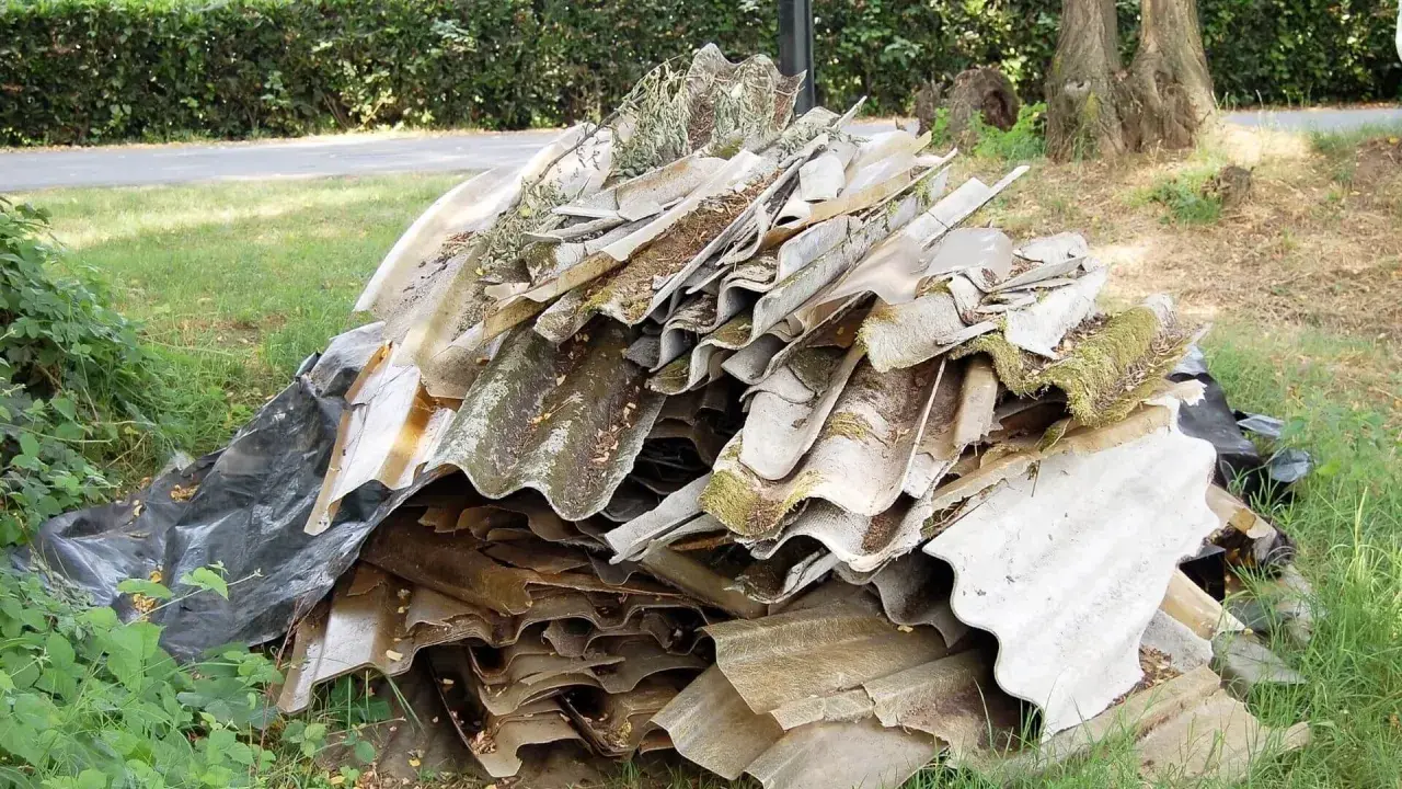 Ein Haufen alter Wellplatten, einst aus faserzement gefertigt, liegt auf einer Wiese. Moos und Schmutz bedecken die verwitterten Oberflächen.