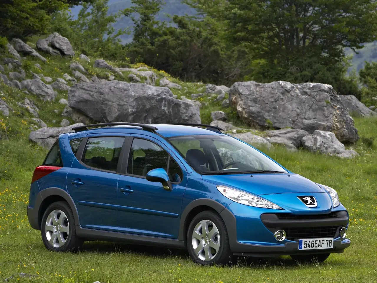 Niebieski Peugeot 207 SW na tle skalistego, zielonego krajobrazu. Idealny na wycieczkę poza miasto.