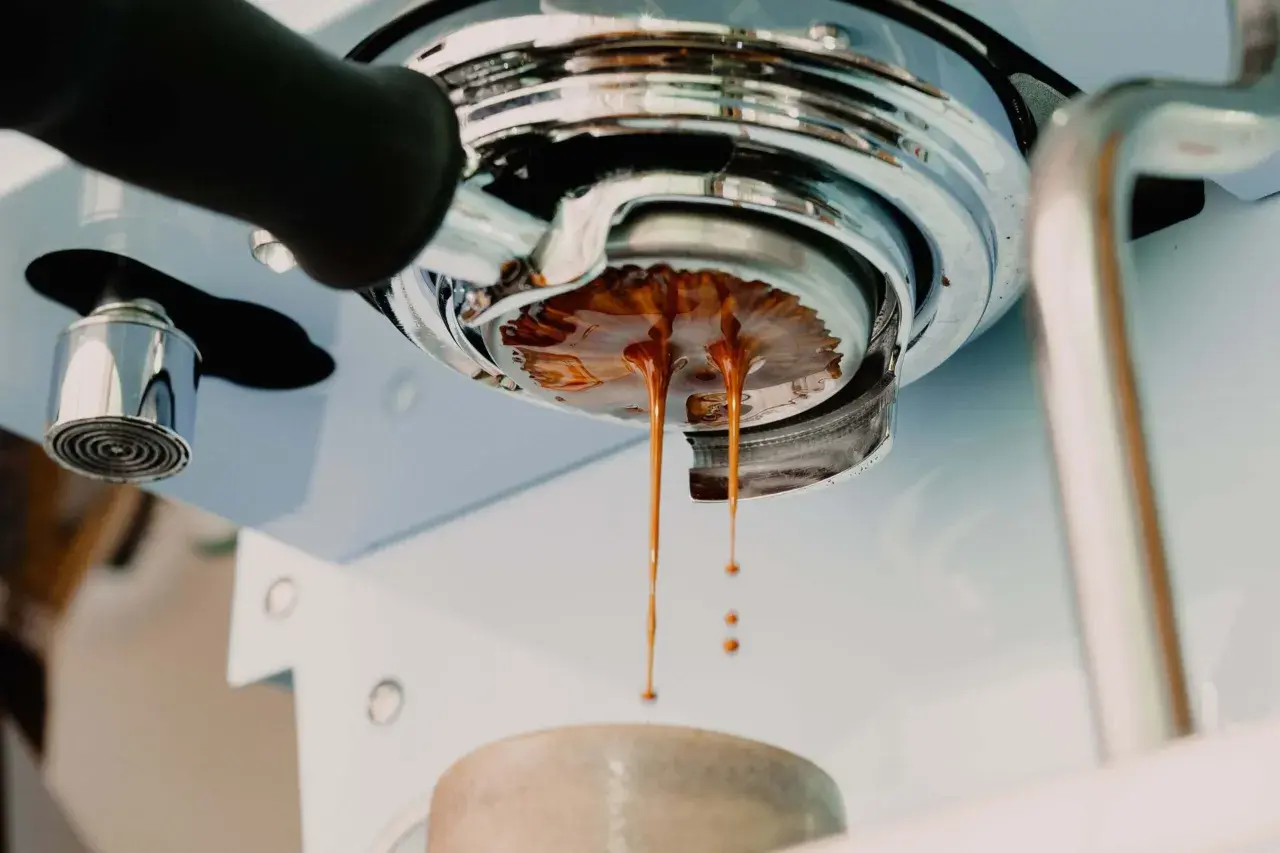 Frisch gebrühter Espresso tropft aus der Siebträgermaschine. Der goldbraune Strahl deutet auf ein perfektes espresso ratio hin.