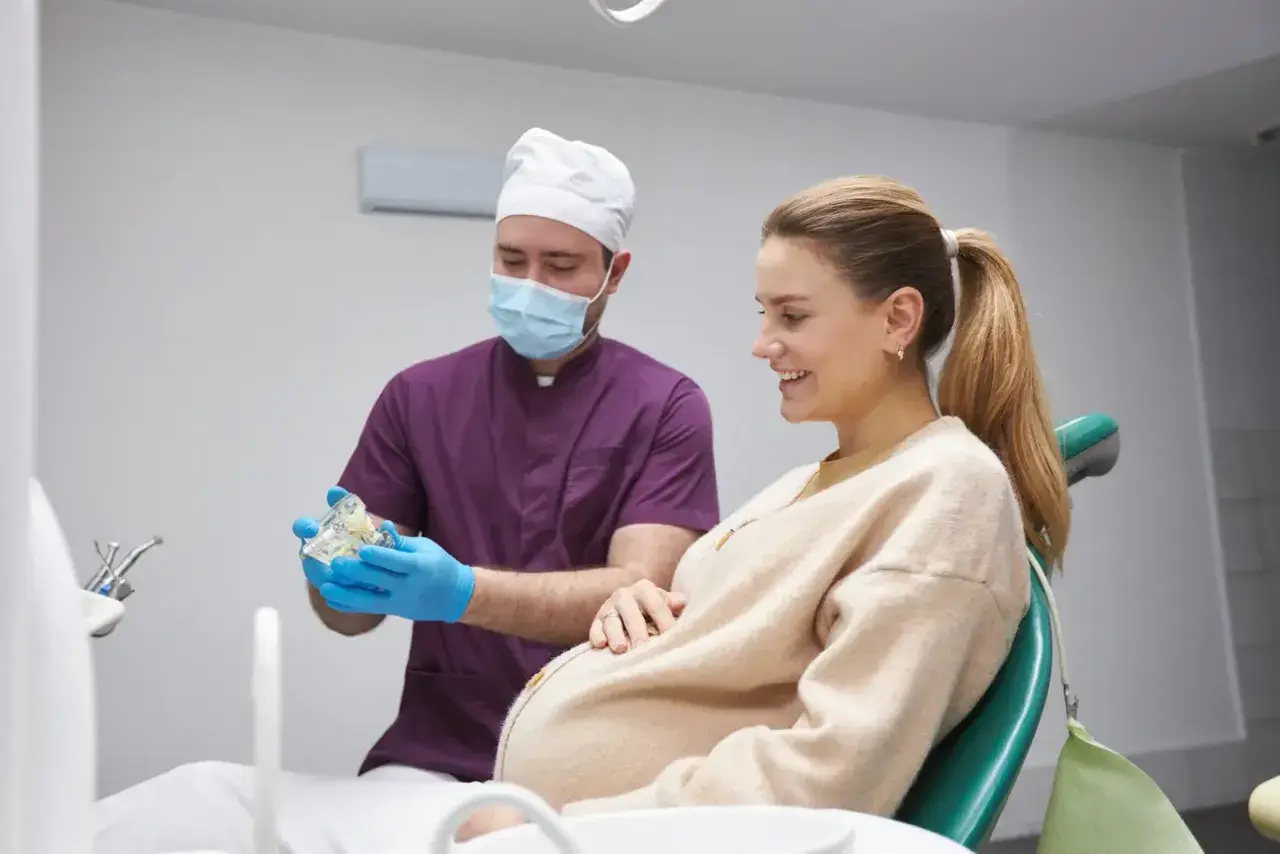 Dentysta wyjaśnia ciężarnej pacjentce procedurę leczenia kanałowego, pokazując model zębów.