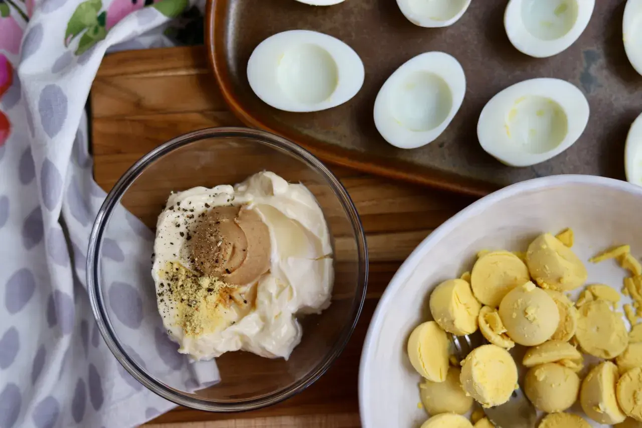 Ingredients for miso egg salad: mayonnaise, miso paste, pepper, and separated egg yolks in a bowl. Halved hard-boiled eggs are on a tray.