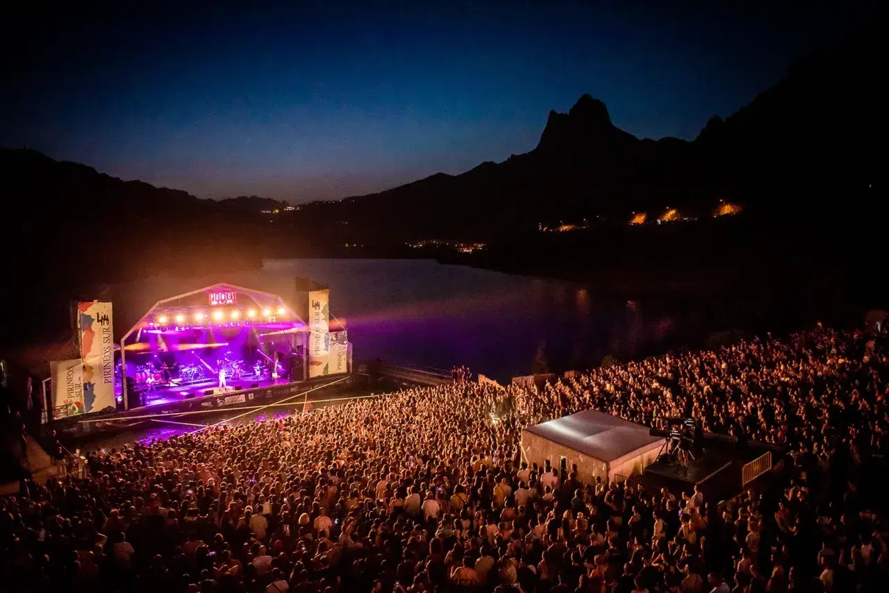 Gran concierto nocturno en el Pirineos Sur. Un mar de gente disfruta de la música bajo un cielo estrellado y montañas.