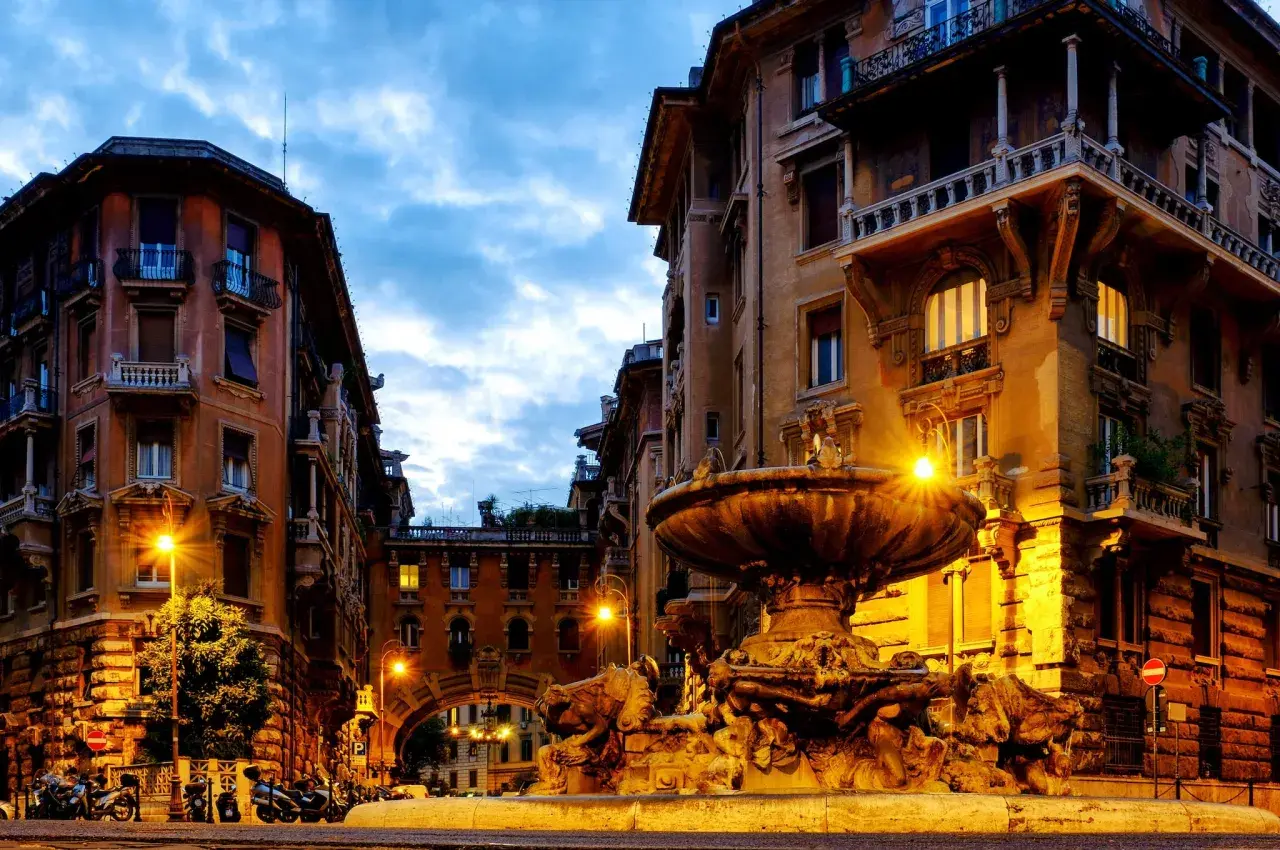 Fontana e palazzi illuminati a Roma, quartiere Coppedè cosa vedere. Atmosfera magica al crepuscolo.