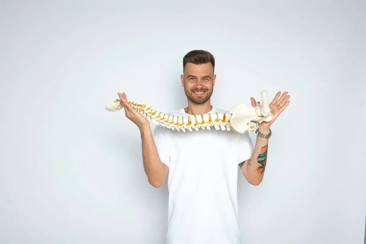Uśmiechnięty mężczyzna trzyma model kręgosłupa, wyjaśniając, whiplash co to jest.