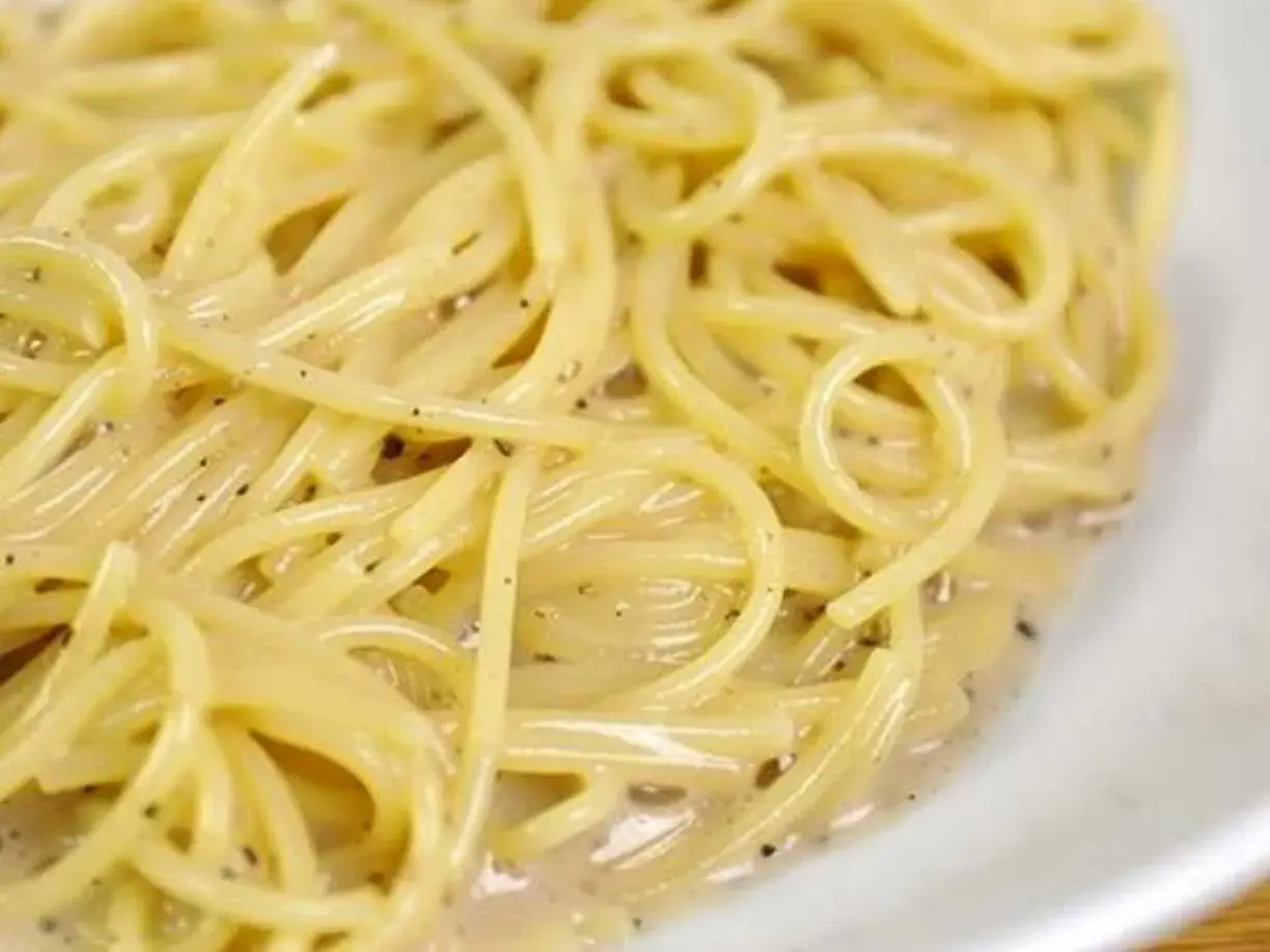En närbild på en krämig portion spaghetti cacio e pepe, med synliga pepparkorn i den lena såsen.
